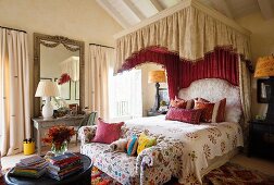 Königliches Bett mit prunkvollem Baldachin, orientalisch gemusterten Kissen und gepolstertem Kopfende; im Vordergrund eine einfache Couch mit Blumenmuster und bunten Zierkissen