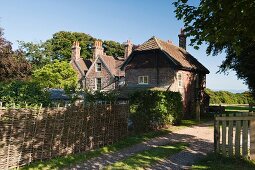 Zufahrtsweg zu traditionellem, englischem Herrenhaus mit Flechtzaun als Gartenabgrenzung