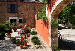 Blumentöpfe auf Kiesboden in mediterranem Garten einer Landhausvilla und Blick durch offenen Torbogen auf die Auffahrt