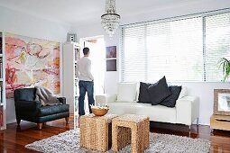 Sitzgruppe im Wohnzimmer mit Vintage Ledersessel und geflochtenen Beistelltischen; junger Mann am Fenster