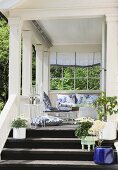 Summery wooden veranda with comfortable furniture and potted flowering plants