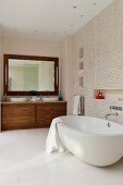 Spacious bathroom with spotlights in ceiling above oval bathtub, washstand area with exotic wood base cabinet and mirror with lamps on either side
