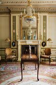 Table with bronze elements in front of fireplace with neoclassical, gilt stucco ornamentation; reflections of endless crystal chandeliers in two mirrors