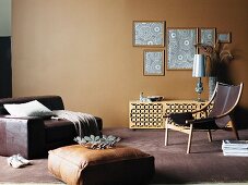 Modern living room in various shade of brown with floor cushion in front of huge leather armchair and framed wallpaper samples on wall