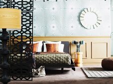 Stehleuchte und Raumteiler seitlich vor Doppelbett an Holzverkleidung in Brüstungshöhe darüber Tapete mit Opart-Muster an Wand