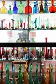 Collection of coloured glass bottles and vases on glass partition shelving