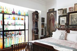 Religious pictures and statues around head of bed and coloured glass bottles in glass partition