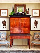 Antique mahogany bureau flanked by Baroque armchairs and framed pictures on wall