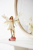 A fairy figurine in front of an oval mirror on a shelf