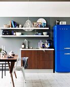 White shelves above wood-effect sink unit next to bright blue fridge