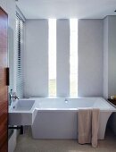 Elegant minimalistisches Bad mit Edelholztür und Lichtschlitzen hinter der freistehenden Designerwanne