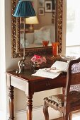 Reading area with antique bureau and wooden chair below gilt-framed mirror