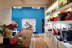 Blick über Theke und Küchenzeile mit rustikaler Arbeitsplatte in offener Küche vor blau getöntem Essbereich