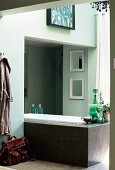 Free-standing, modern bathtub partially built into niche in bathroom painted pale green