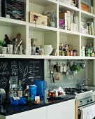 Items stored on open shelving unit above hob and sink in contemporary kitchen with chalkboard