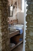 View past rustic stone wall of washstand with twin basin in bathroom
