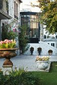 Conservatory abutting house between stone facades; well-kept lawn and decorative planters in foreground