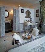 View from double bed past breakfast tray on ornate bench to bathroom partitioned by grey, folding doors