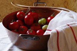 Tomatoes in a copper bowl with a tea towel and a wooden spoon
