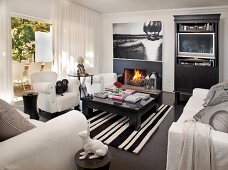 Black and white living room; white sofa set and black coffee table on striped rug in front of open fireplace with large photograph of child on wall