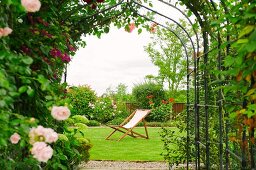 View of deckchair through archway covered in flowering roses