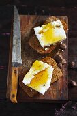 Two wholemeal rolls topped with cottage cheese and honey on a wooden board with a knife