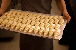 Person hält Backblech mit ungebackenen Croissants