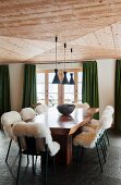 Lammfell auf Stühlen um rustikalem Holztisch und grüne Vorhänge am Fenster im Esszimmer mit Holzdecke