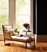 Inviting reading area in front of French windows with scatter cushions on antique chaise longue and side table