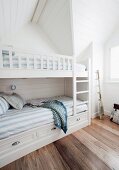 Bedroom with white bunk beds and blue and white striped bed linen in attic room with dark wooden floor