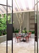 View of retro-style, coloured, metal chairs at round table in courtyard through open terrace door