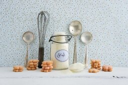 A whisk, a silver spoon, a flip-top jar, semolina and biscuits