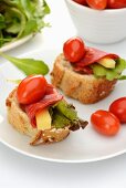 Baguette slices topped with cheese, chorizo, lettuce and date tomatoes