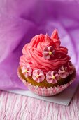 A cupcake decorated with red frosting and sugar flowers