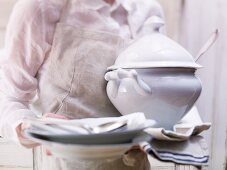 A man holding a soup tureen, crockery and cutlery