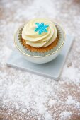 A cupcake decorated with light frosting and a sugar snowflake in a cup