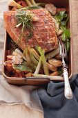Crispy roast pork on a bed of oven-roasted vegetables in a roasting tin
