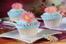 Light blue cupcakes decorated with pink flowers and sugar balls