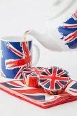 Tea being poured from a Union Jack teapot with matching cupcakes