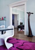 View through suite of rooms from dining area into living room; white 60s classic chairs on bright rug with giraffe sculpture in background