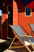 Liegestühle auf Terrasse vor rotbraun gestrichenem Holzhaus