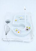 Floating daisies and lit birthday candle in white china dish in the shape of a number