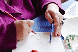 Hände mit rotem und blauem Farbstift beim entwerfen eines Musters auf Papier