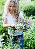 Blondes Mädchen pflückt blühende Kräuter im Garten