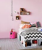 Bed with storage compartments below, small decorative shells on wall and industrial pendant lamps above bedside cabinet in jaunty pink