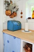 A vintage bread bin and copper cooking and baking utensils, in a renovated kitchen with a pale wood worktop and white wood-panelled walls
