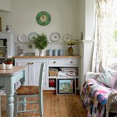Table, rush-bottomed chair and patchwork blanket on wicker sofa in cosy, country-house kitchen