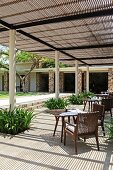 Terrace area under shady pergola with white, round columns, small tables and inviting armchairs for relaxing