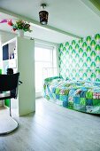 Kinderzimmer mit Raumteilerregal zwischen Bett und Schreibtisch; Blau- und Grüntöne für Patchworkdecke und Retrotapete