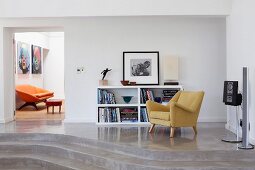 50er Jahre Sessel und halbhohes Regal auf Podest mit Stufen aus Beton und Blick durch offene Tür auf orangefarbenes Sofa